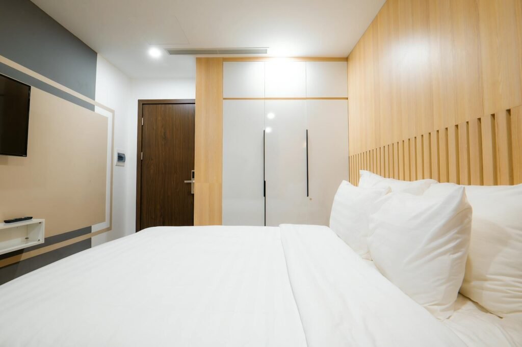 A modern hotel room with minimalist and cozy decor featuring a comfortable bed and wooden panels.